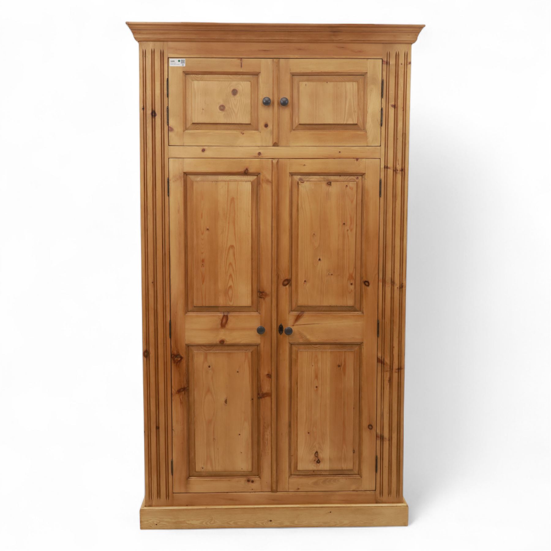 Modern stripped pine double wardrobe, with stepped cornice over upper cupboard doors and two full-height fielded panel doors, fluted stile detailing, ebonised knob handles, and plinth base