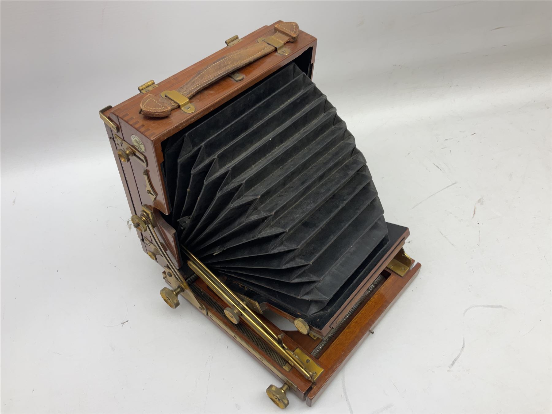 Ensign 'The Sanderson' folding plate camera in mahogany and lacquered brass, field model with canvas wrapped box, two mahogany photographic plates, 'Busch rapid Symmetrical F:8' lens,  and a wooden tripod 