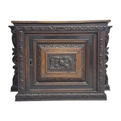 18th century and later carved oak cupboard, enclosed by panelled door carved with central bird motif and scrolled leafage with an outer ebony band, the frieze and uprights carved with repeating lunette and floral designs, flanked by scrolled foliate carved upright brackets