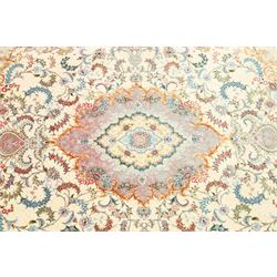 Fine Persian silk inlaid ivory and rose ground Tabriz rug, the busy field decorated with a central foliate pole medallion surrounded by scrolling foliage with trailing flowerheads and bouquets, the multiple guard lines filled with repeating scrolling palmettes and interlocking floral motifs