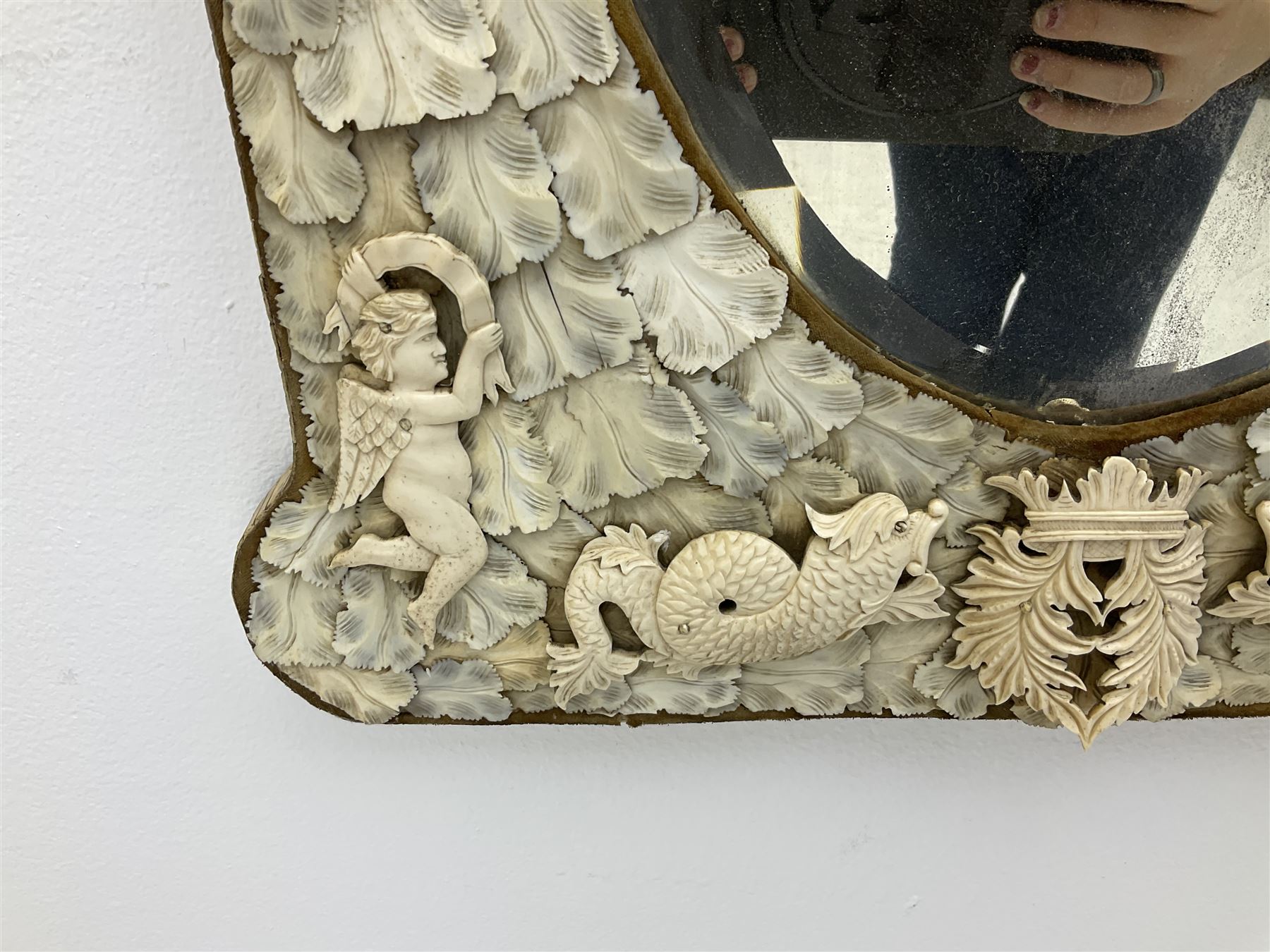 Pair 19th century French Dieppe bone and ivory wall mirrors, the oval bevelled mirror plates within rectangular frames with shaped tops, profusely decorated with ivory leaves, further detailed with carved bone armorial type crest inscribed 'SGOTORVM', putti, fish and mask heads, H81cm W48cm