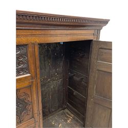 Large 18th century and later oak livery cupboard, projecting moulded and dentil cornice, sunken fillet moulded frame, triple vertical panelled central upright, enclosed by two doors each with five panels, the top row of panels carved with stylised scrolls, the lower panels carved with foliate lozenges, on shaped bracketed skirt base 