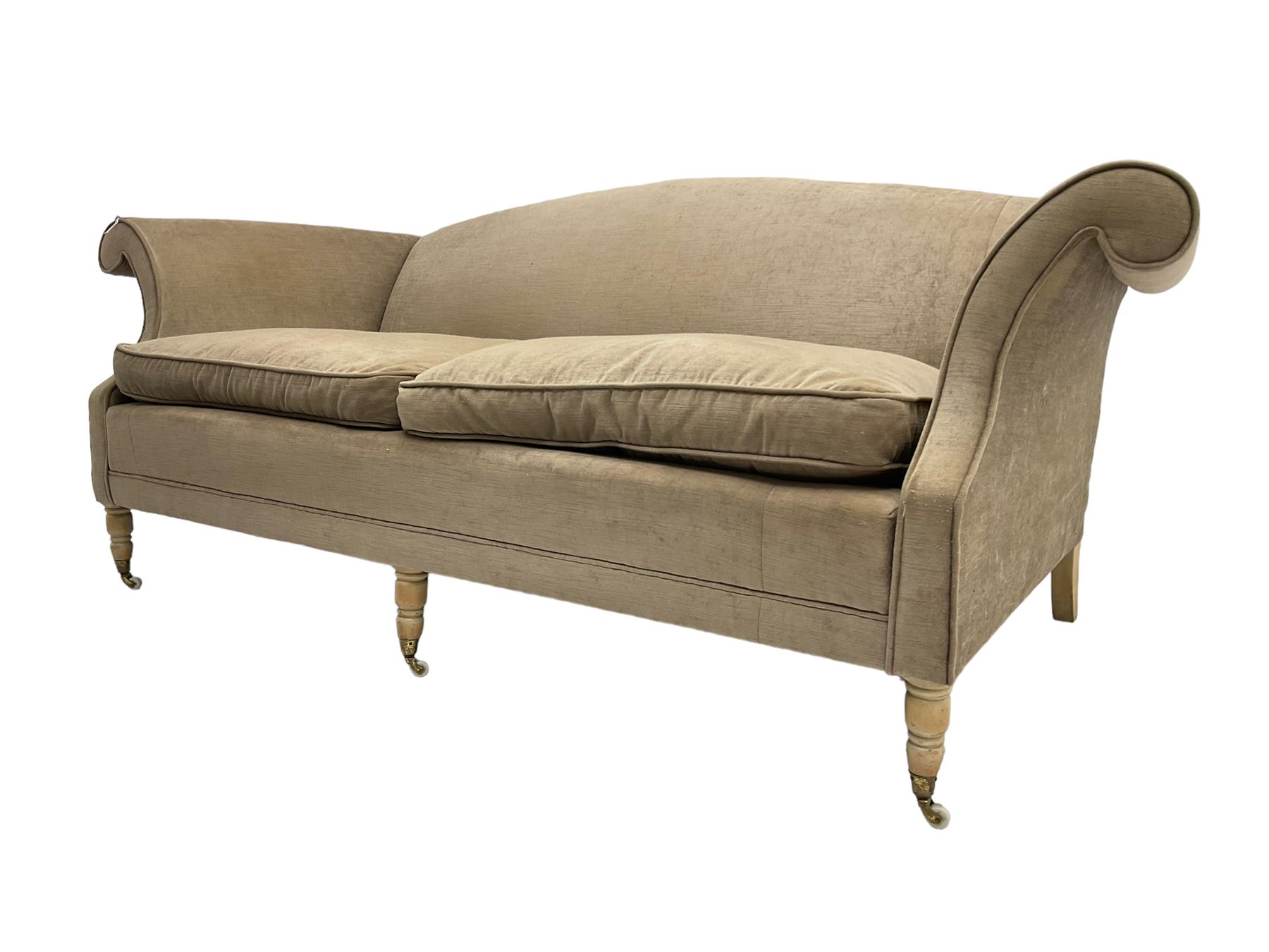 Traditional three seat sofa, curved back over scrolled arms, upholstered in crushed beige fabric with matching loose cushions, on turned front supports with brass and ceramic castors, together with matching footstool