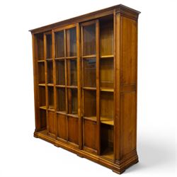 Wesley Barrel - large cherry wood bookcase, with projecting cornice and fielded panelled sides, with three sections comprising three fixed shelves, sliding glazed and panelled doors, moulded plinth base