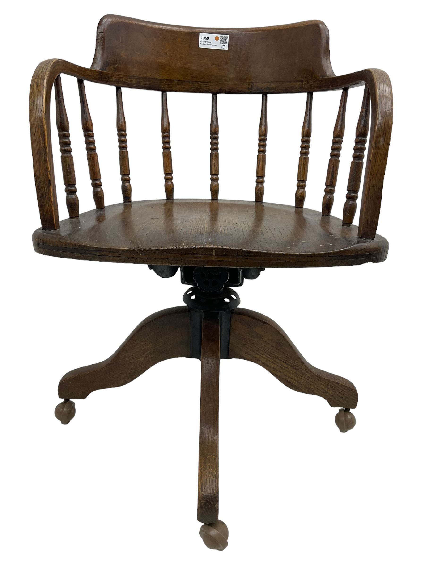 Early 20th century oak framed swivel Captain's chair, tub shaped back with turned spindle supports over saddle shaped seat, quadriform base on castors