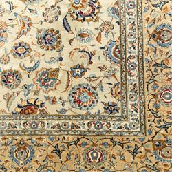 Central Persian Kashan hand-knotted carpet, cream ground with radiating floral rosette medallion in soft blue and terracotta, the field filled with stylised blooms, cloudband vines and palmette motifs, enclosed by triple borders featuring lotus and boteh designs, with cotton fringe ends 