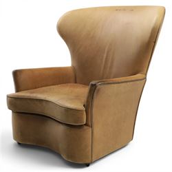 20th century tan leather armchair, the curved wing back above low square arms, shaped loose seat cushion with piped edge, close-nailed side detail, raised on concealed castors