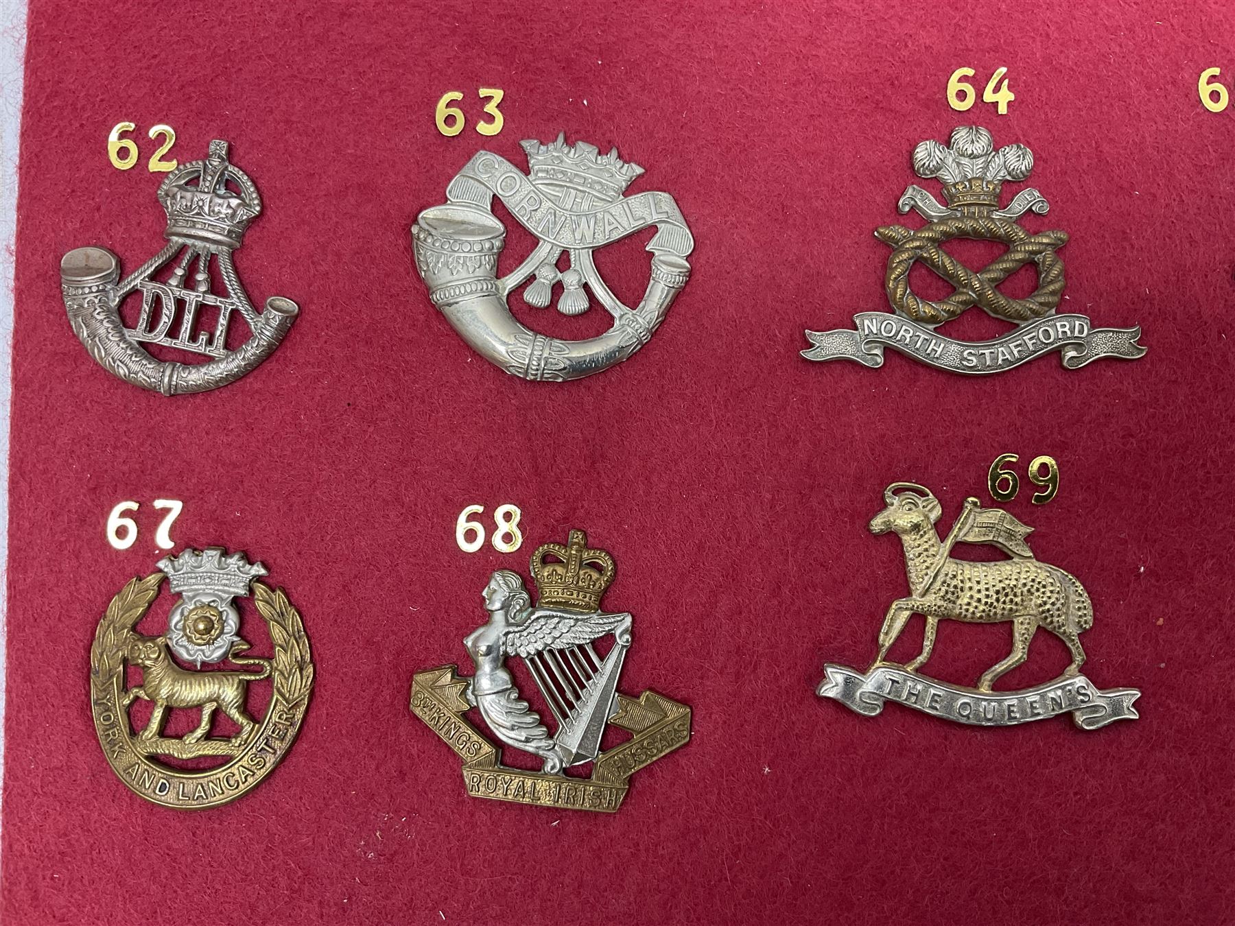 Twenty cap badges including Welsh Guards, Kings Royal Irish Hussars, York & Lancaster,  Loyal Suffolk Hussars, North Stafford, Durham Light Infantry, Cheshire, West Yorkshire, Norfolk, South Wales Borderers, Dorsetshire etc; mounted on a board for display