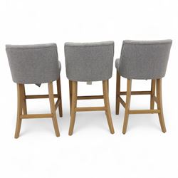 Contemporary set of three upholstered bar stools, each with button-tufted grey fabric backrest and seat, raised on light oak finish square legs united by stretchers