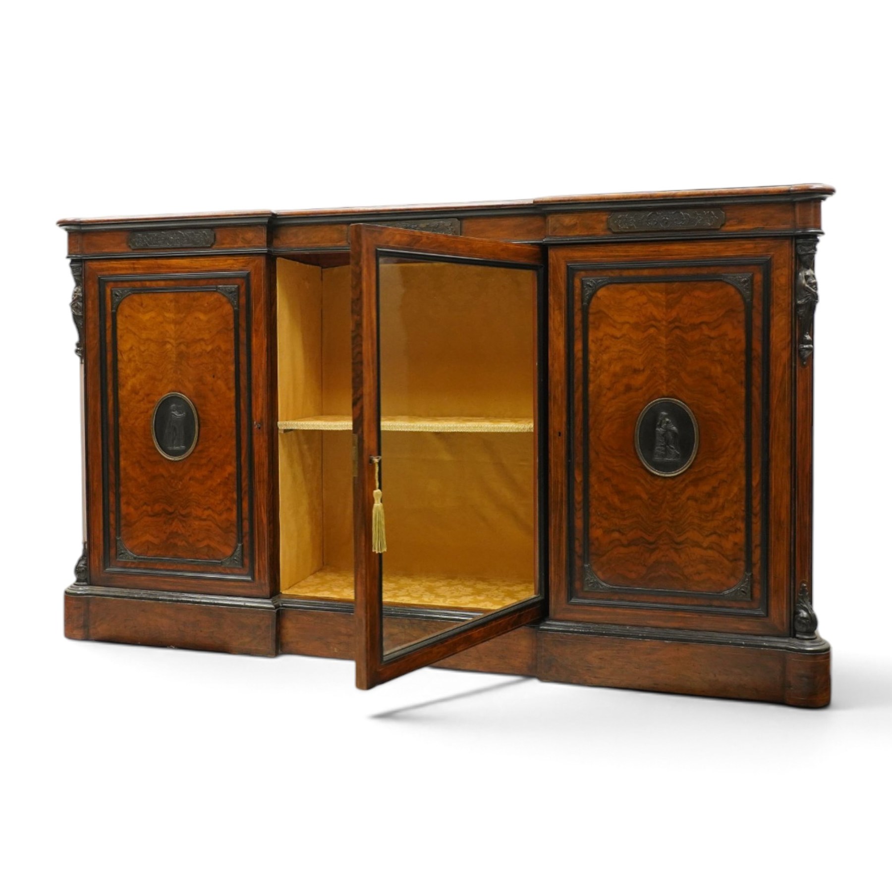 Lamb of Manchester (est. 1843) - Victorian Aesthetic Movement inlaid figured and burr walnut inverted-breakfront credenza, the shaped rectangular top with ebony banding and boxwood stringing, the frieze applied with bronze mounts decorated with foliate and scroll motifs, fitted with central glazed door flanked by panelled doors with central oval metal plaques depicting Classical Muses with lyre, the flanking canted uprights applied with caryatid maidens holding torches, acanthus terminal over skirted base