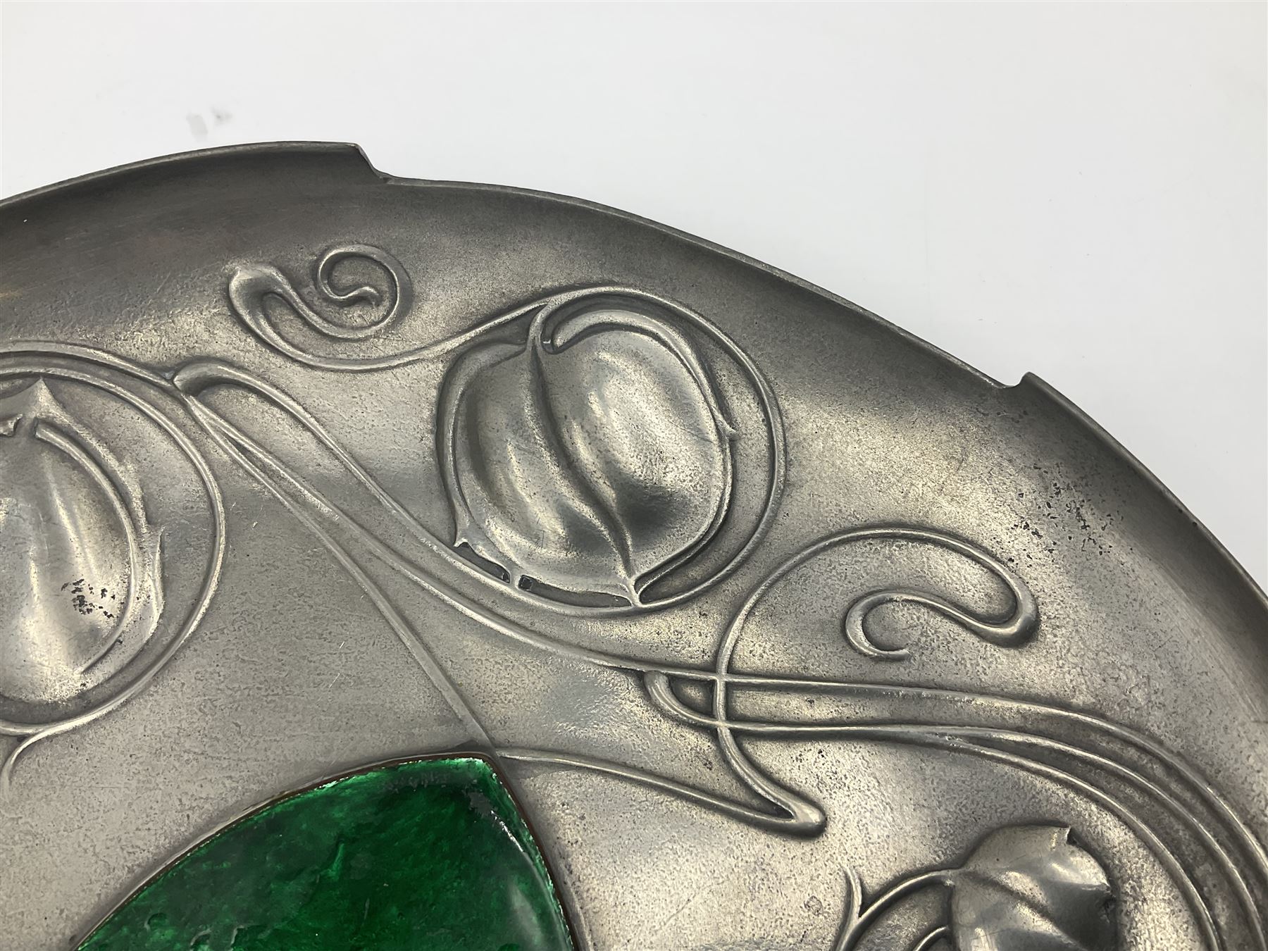 Liberty & Co Tudric pewter Bollelin tray, designed by Archibald Knox, of circular form with shaped edge, cast in relief with foliate tendrils surrounding a green enamel cartouche, impressed beneath Made by Library & Co English Pewter 044, D25.5cm