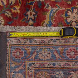 Central Persian Kashan hand-knotted carpet, madder red field with a central cusped medallion of ivory and deep indigo ground, enclosing a stylized floral rosette, framed by scrolling arabesques, field richly ornamented with an intricate network of flowering vinery, palmettes, and delicate floral sprays, spandrels in deep indigo, principal border of navy ground decorated with a continuous palmette and vine-scroll, flanked by multiple guard stripes, with cotton fringe ends 