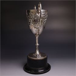 Edwardian silver twin-handled trophy, with embossed floral and scrolling decoration, upon a knopped stem and circular foot, hallmarked Goldsmiths & Silversmiths Co Ltd, London 1903, upon a black plinth, including plinth and handles H32cm