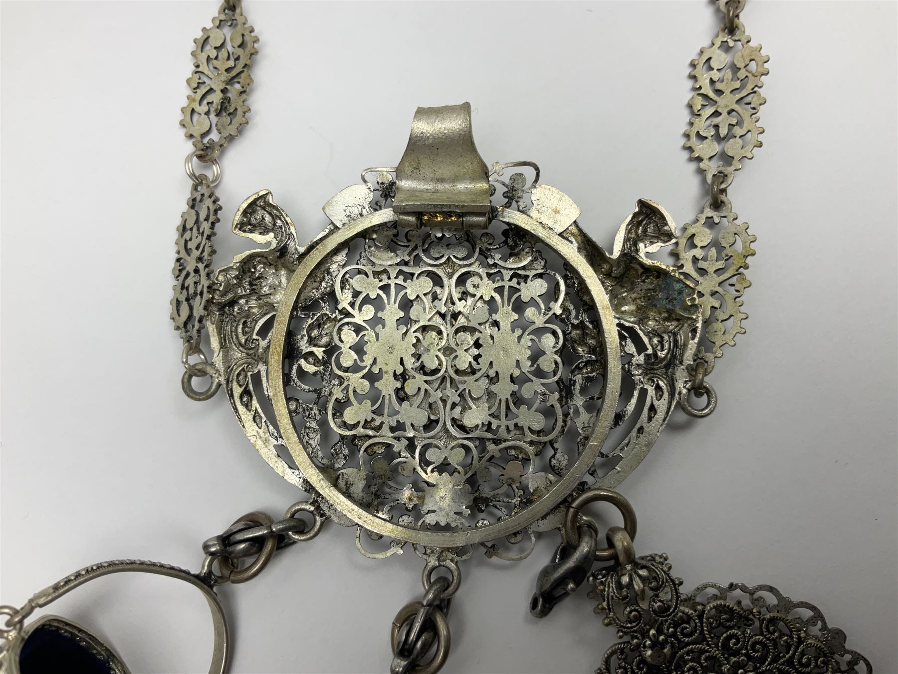 19th century continental silver plated chatelaine, the main body flanked with winged mythical beasts and central soldier slaying a dragon supporting three suspended items to include velvet lined small basket and long clasped filigree chain, together with a thimble