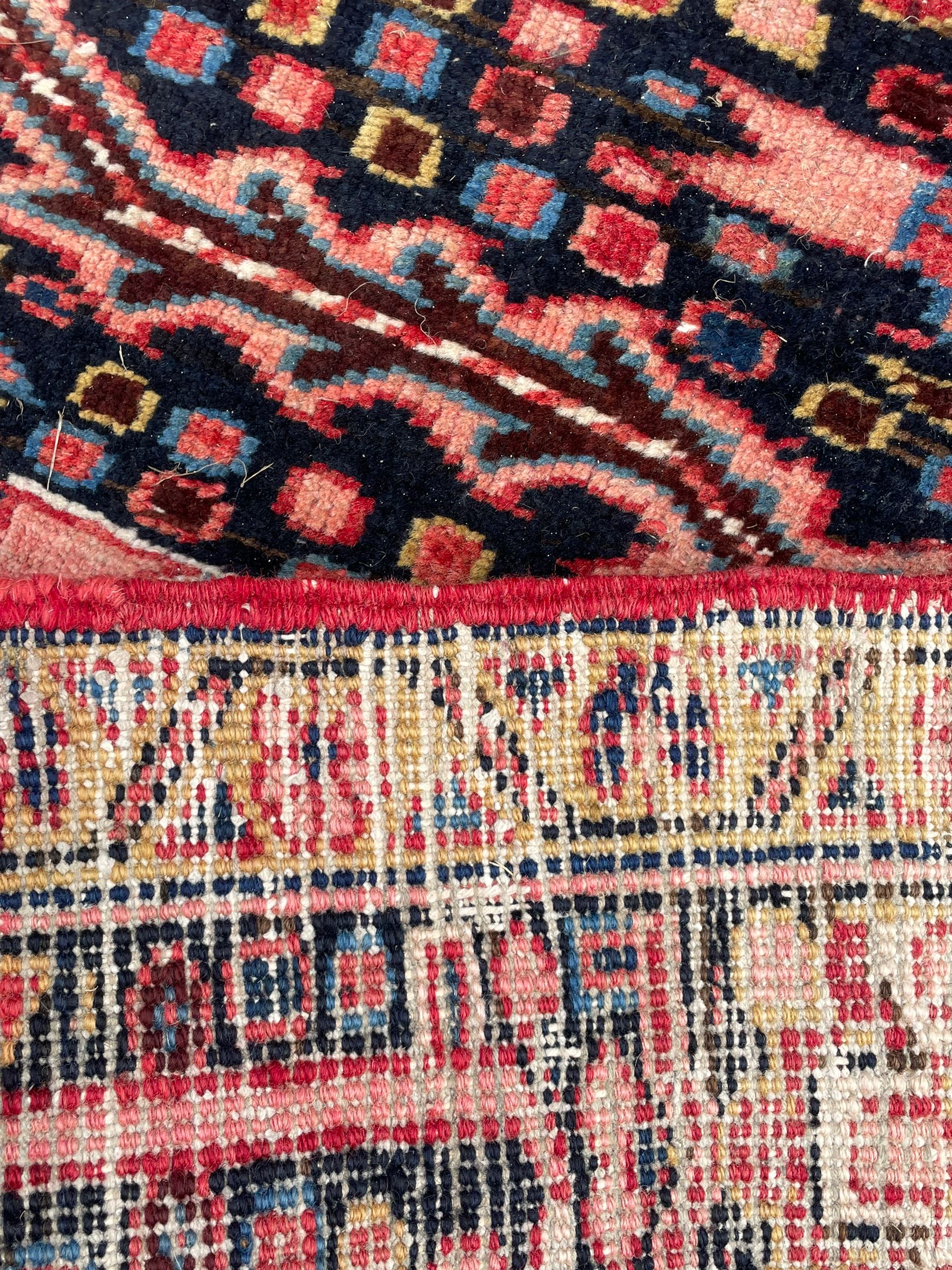 Antique Persian coral ground carpet, the large central floral pole medallion with extending foliate designs, the thick guarded indigo border with repeating flower heads and circles