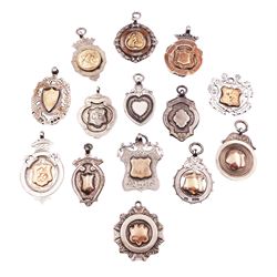 Fourteen silver fobs of various form, mostly early 20th century examples to include a fold faced example detailed with a figure kicking a ball, within a border detailed with orange enamel panels, hallmarked Birmingham 1928, a number of other gold facing examples, and four double sided examples, various hallmarks, dates ranging 1892 to 1950, approximate total weight 4.05 ozt (126 grams)