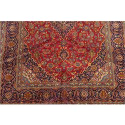 Persian Kashan hand-knotted carpet, madder red ground centred by shaped dark navy, ivory and pale blue floral medallion with pendants, surrounded by scrolling vines, palmettes and flowerheads, dark navy spandrels, enclosed by dark navy floral border with multiple floral guard stripes