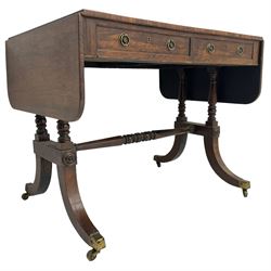 Regency rosewood sofa table, drop leaf rectangular top with rounded corners, fitted with two drawers and two opposing false drawers, raised on dual turned columns terminating in splayed feet united by turned stretcher, on brass cups and castors