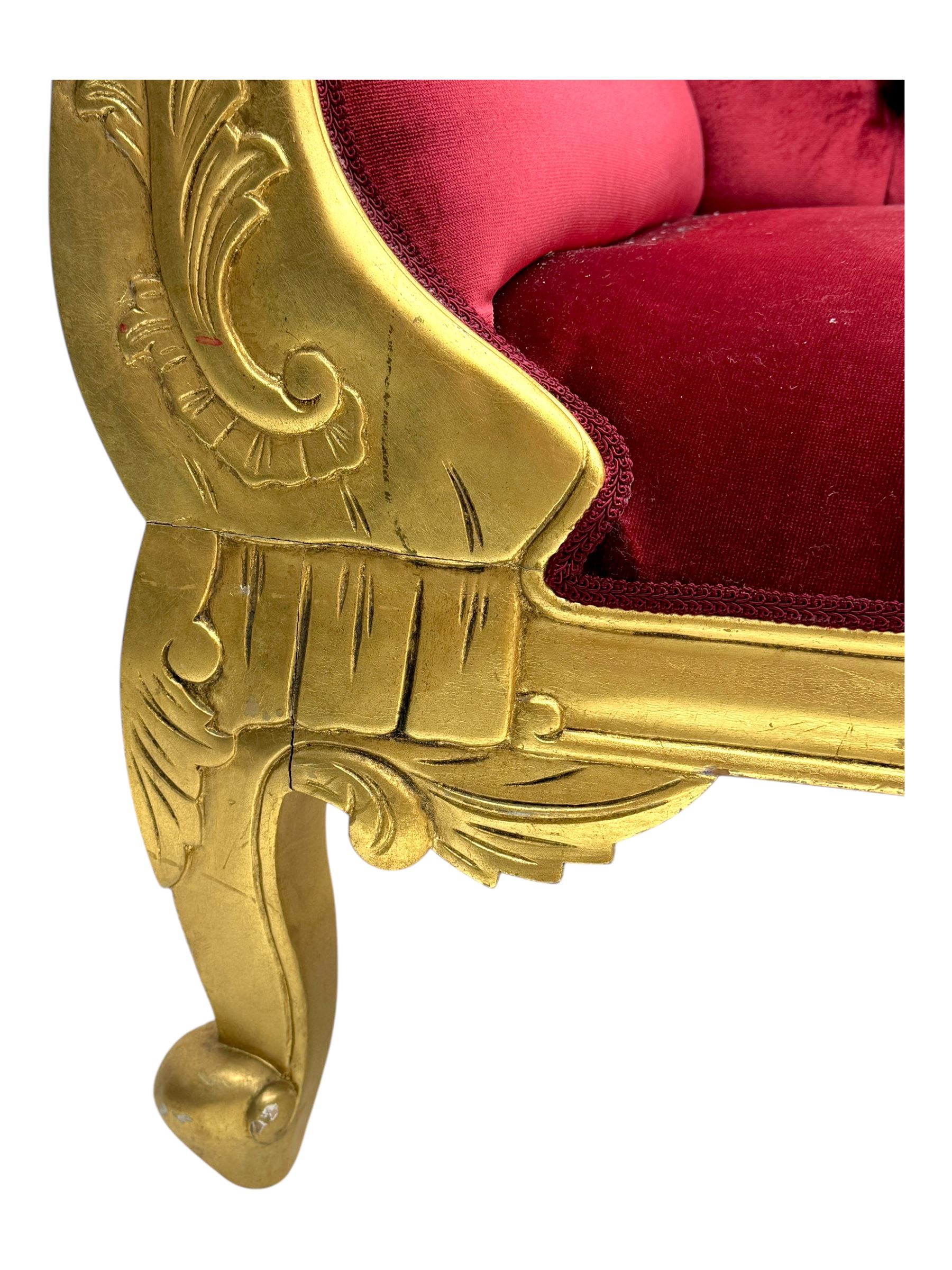 Victorian design giltwood chaise longue, the curved backrest and seat upholstered in deep red velvet with tufted detailing, the frame carved with floral motifs and scrolling acanthus leaves, raised on shaped cabriole supports