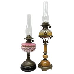 Two late 19th/early 20th century oil lamps, comprising example with pink glass reservoir painted with roses, together with oak based oil lamp with cut glass reservoir supported by ornate brass supports, both with chimneys, largest H74cm