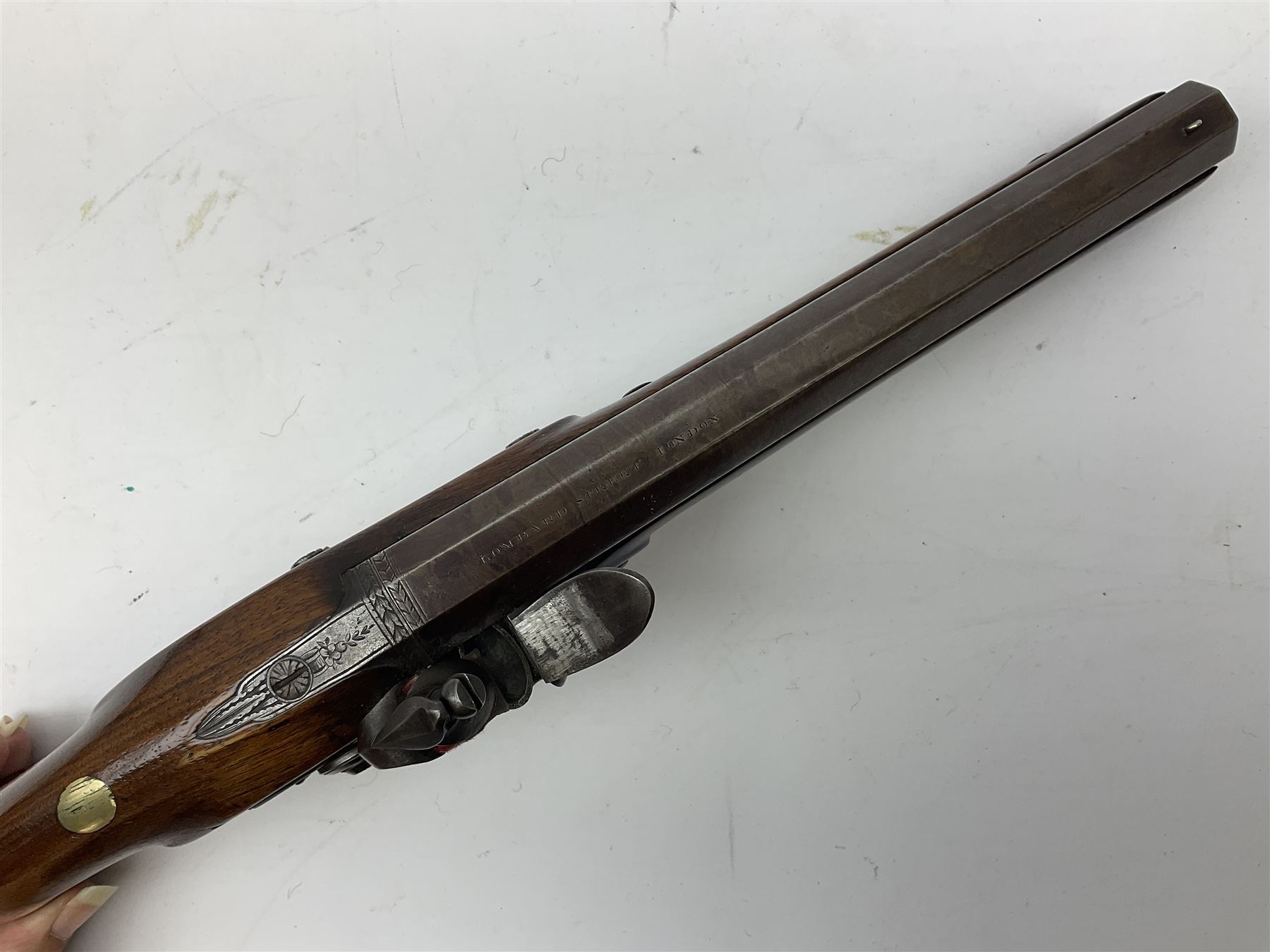 Early 19th century flintlock 16-bore overcoat/duelling pistol by William Bond Lombard Street London, the 23cm octagonal brown stub twist damascus barrel with small foresight, two barrel pins and ram rod under, inscribed Lombard Street London to the top and W. Bond to the action, full walnut stock with lightly engraved steel furniture, pineapple finial and escutcheon, half cock facility L39cm; loose mounted on later mahogany display stand with trade label