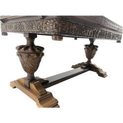 Early 20th century West Yorkshire carved oak dining set - the table with rectangular drawer leaf extending top, the skirt relief carved with flowers and foliage, on twin urn shaped pedestals with lobe carved tops and acanthus leaf bodies, on platform stretcher base (99cm x 153cm - 245cm, H87cm), and set six dining chairs,  high arched backs relief carved with c-scrolls and flower heads, upholstered in brown faux leather, the front supports matching the table pedestals