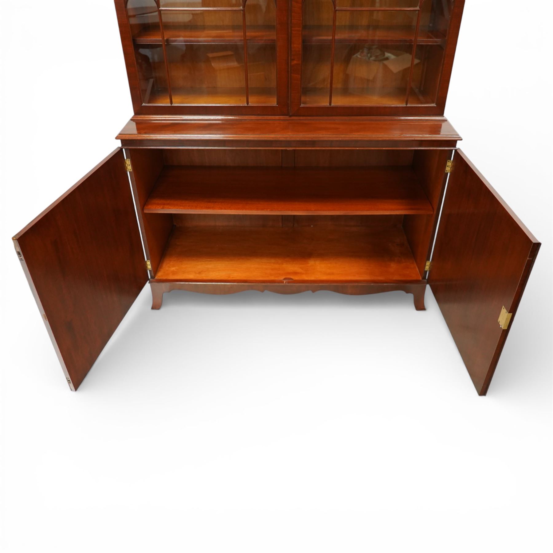 William Tillman - Early 20th century mahogany display cabinet, moulded cornice above a frieze carved with roundels and fluting, pair of astragal glazed doors enclosing adjustable shelving, the lower section fitted with twin panelled cupboard doors centred with oval veneered panels, shaped apron and bracket feet