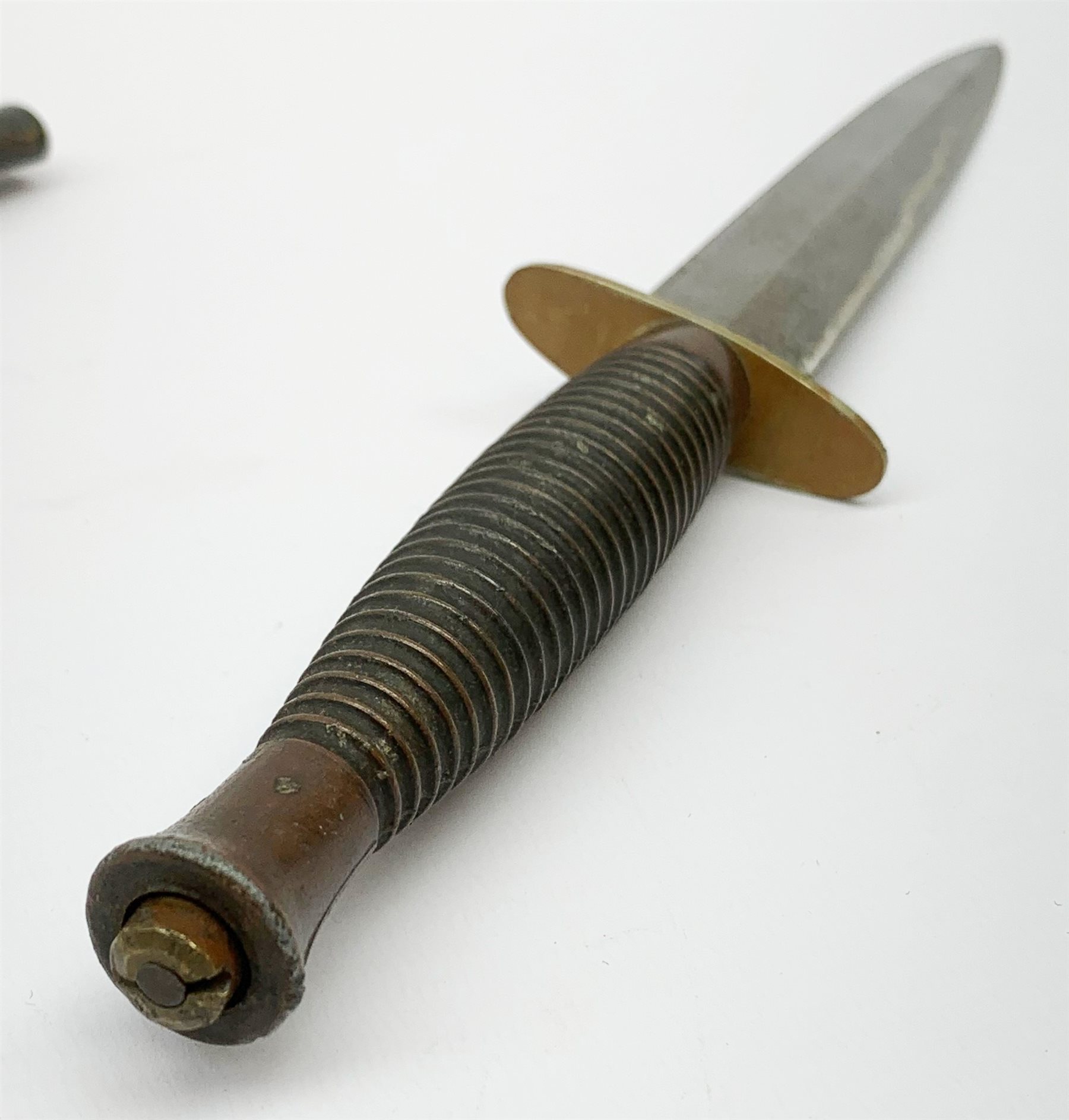 British Fairbairn-Sykes type 3rd pattern Commando fighting knife with unmarked 17cm double edged blade, oval brass cross-guard and ringed grip, in brown leather scabbard 32cm overall