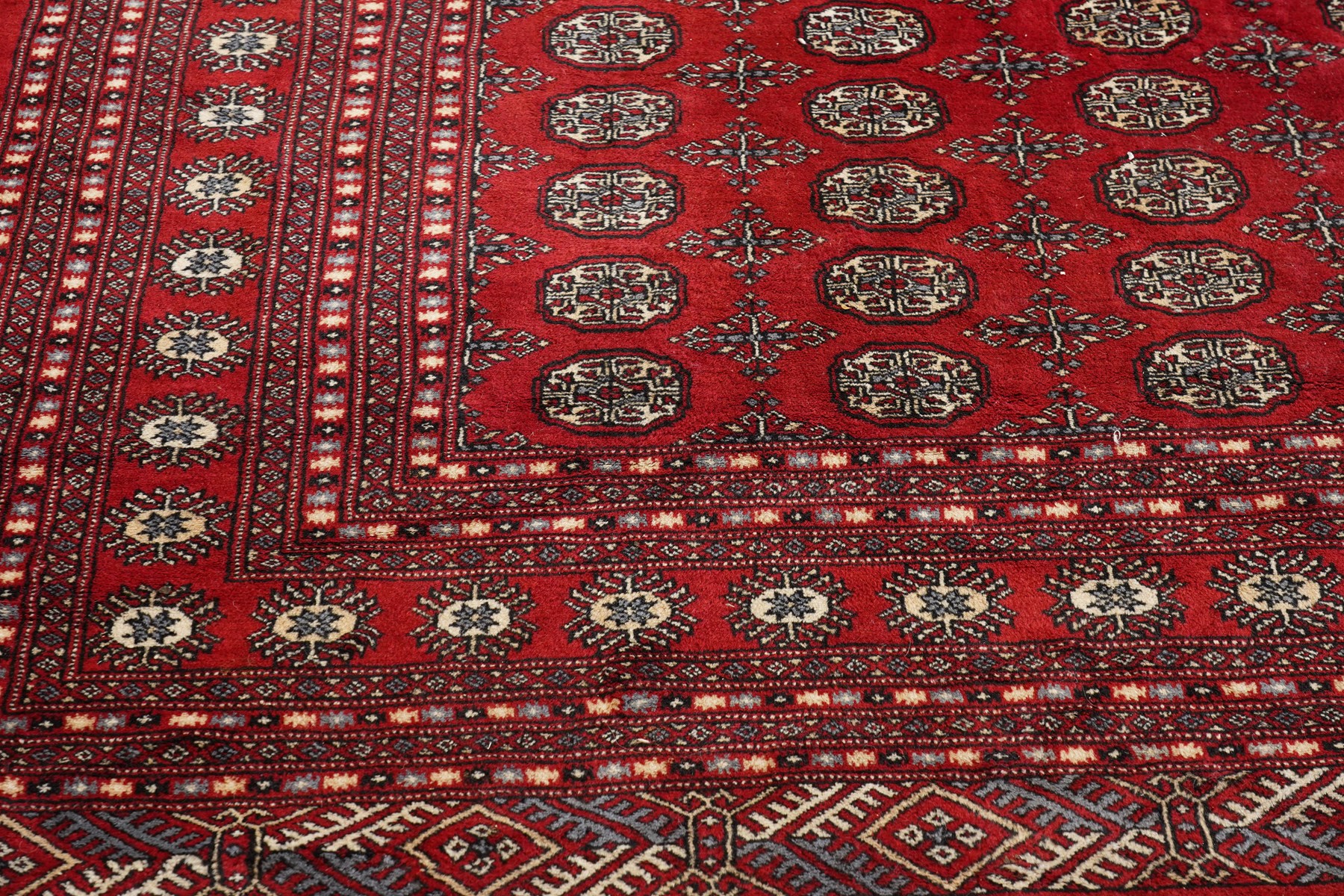 Large crimson ground Afghan Bokhara carpet, the field decorated with repeating Gul and geometric motifs, the multiple guard stripes with further geometric decoration