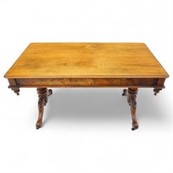Mid Victorian walnut library table, plain top of rectangular form with moulded edge above frieze fitted with opposing drawers, table supported on a pair of turned and hexagonal carved baluster end standards, united by a turned stretcher terminating in scrolling sabre legs carved with acanthus and floral details, resting on ceramic castors, circa 1860