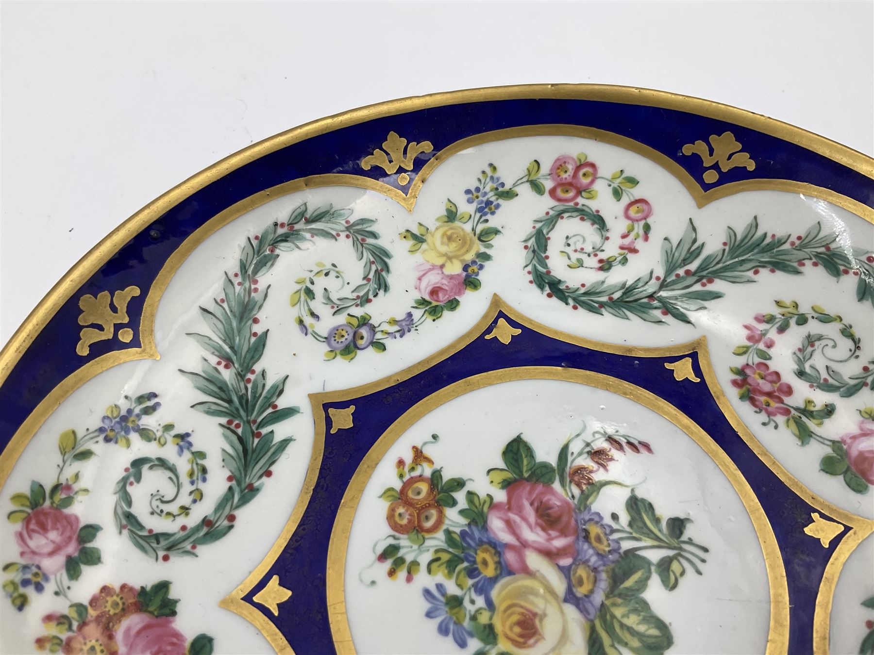 19th Sèvres style porcelain cup and saucer, the cup painted with a figural scene, against a scalloped border of scrolling floral swags on a blue ground, together with a Sèvres soft paste porcelain coffee can and saucer, painted with panels of exotic birds, roses and a border of cornflowers, LL monogram enclosing date letters H above painters mark, coffee can H6.5cm, saucer D13.5cm (2)