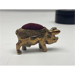 Three pin cushions, comprising gilt metal pig, silver plate shoe, circular pin cushion on threel feet, together with black pin holder with silver writing to the lid 