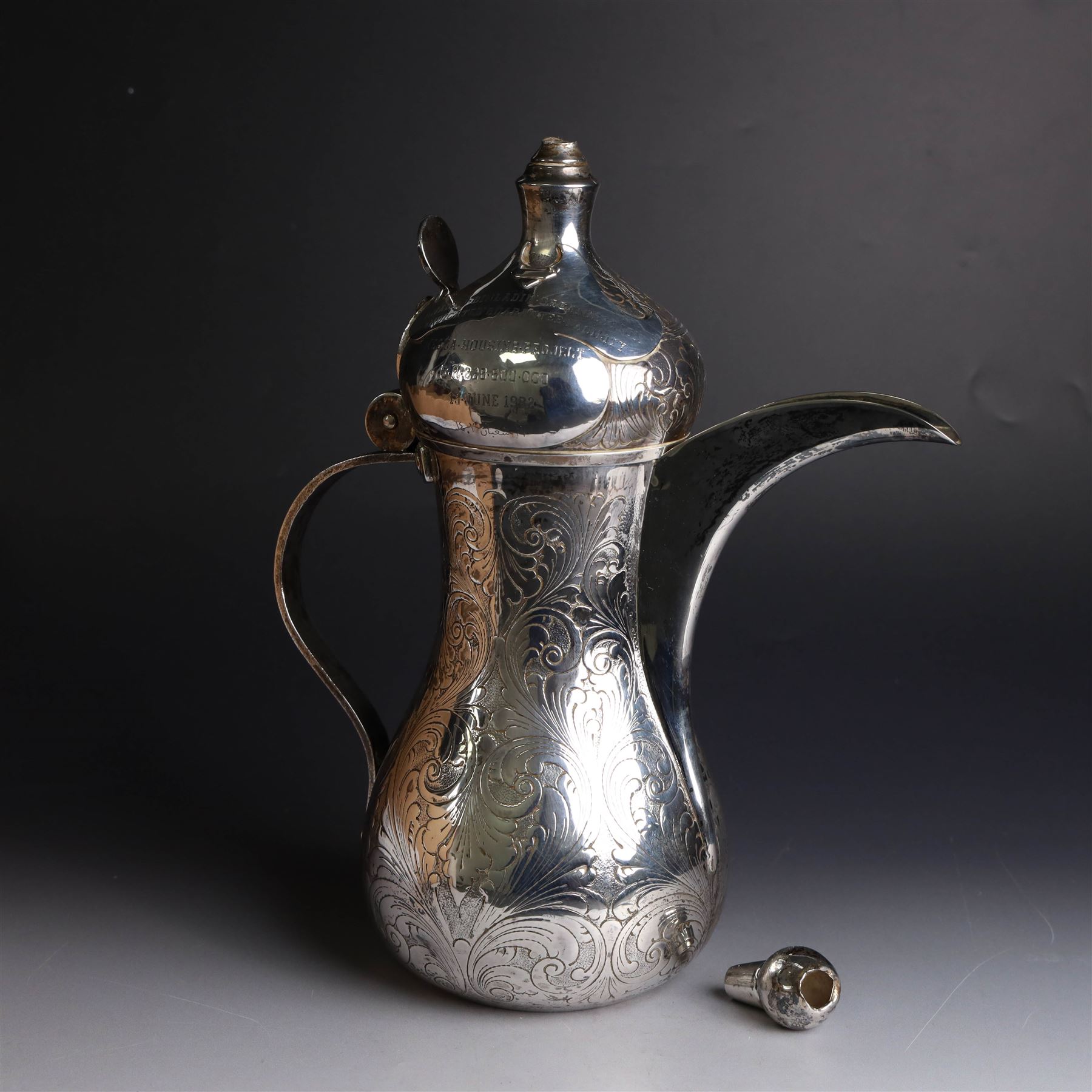 Middle Eastern silver coffee pot or Dallah, of baluster form with elongated spout and domed lid, with chased scrolling foliate decoration, the lid with applied silver plaque with presentation engraving, stamped 925 to base, H26.5cm