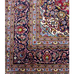Central Persian Kashan hand-knotted carpet, the madder red field with central lobed medallion in indigo and ivory, enclosing scrolling arabesques and flowerheads, framed by palmette spandrels and an indigo border of rosettes and lotus forms between multiple floral guard stripes, from the region of Kashan