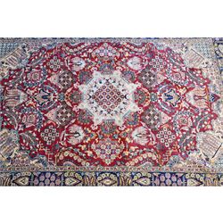 Central Persian Najafabad hand-knotted carpet, crimson field with a central elaborate cusped medallion with radiating floral motifs, surrounded by finely drawn scrolling vines incorporating stylized palmettes and rosettes, flowering plants and vase motifs, ivory spandrels similarly decorated enclosed by a dark indigo main border of floral arabesques between multiple guard stripes, with cotton fringe ends 