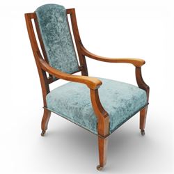 Arts & Crafts mahogany framed armchair, shaped rectangular back with open uprights, padded back, seat and arm supports upholstered in blue velvet, downswept arms on square tapering front supports with brass caps and castors, the rear supports slightly splayed