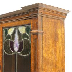 Arts and Crafts oak dresser, projecting moulded cornice above three glazed panels with coloured leaded glass floral panels, flanked by two glazed doors enclosing two adjustable shelves, open mirrored recess below with mirrored back, the base fitted with two short drawers over two central drawers flanked by carved panelled cupboard doors, ornate brass handles, raised on tapering square legs