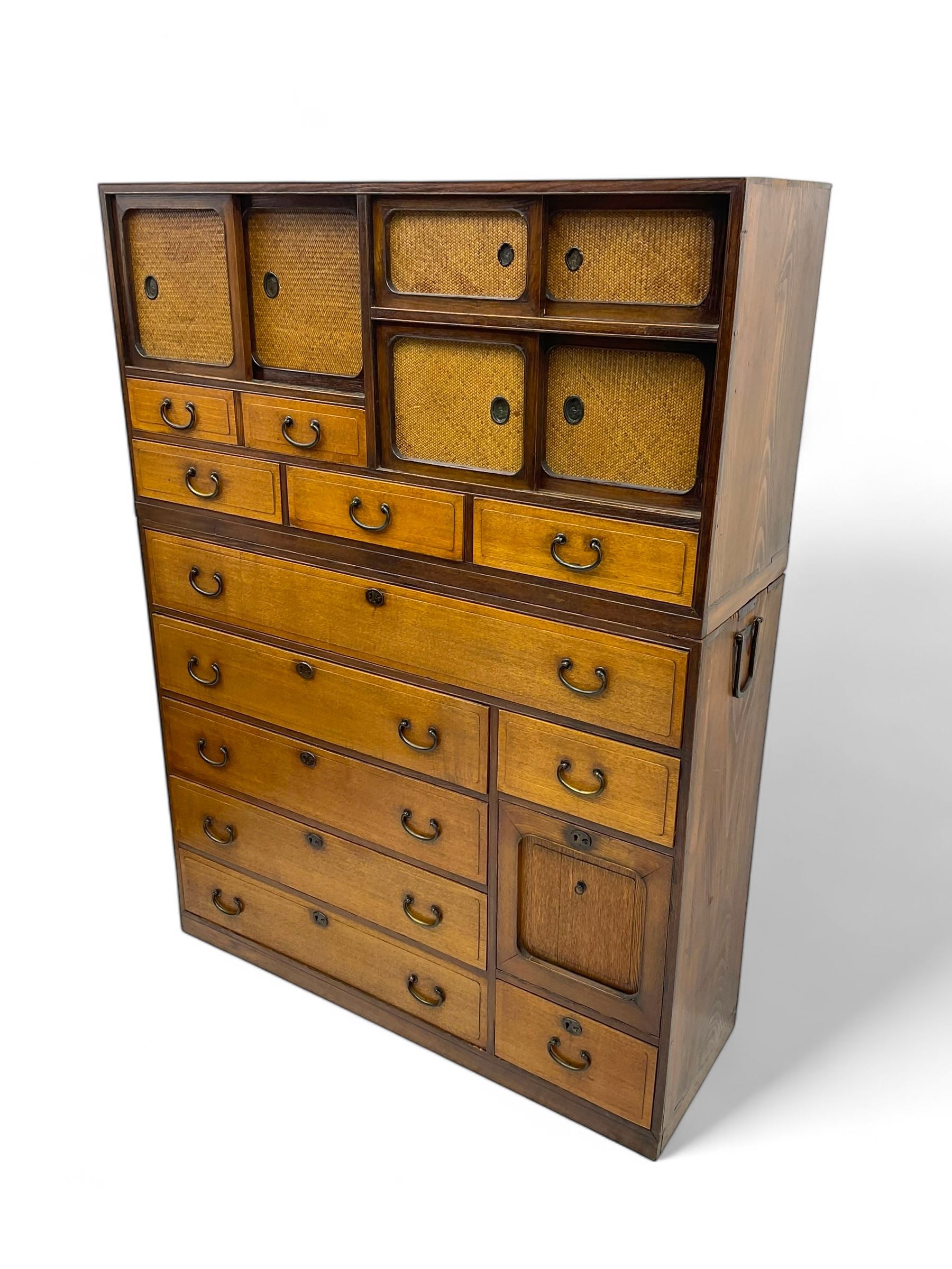 Late Meiji-period Japanese keyaki wood tansu chest, upper section with six sliding woven rattan doors over five drawers, lower section fitted with an asymmetrical arrangement of seven drawers and side cupboard with a hinged door enclosing three additional drawers, iron drop handles to sides