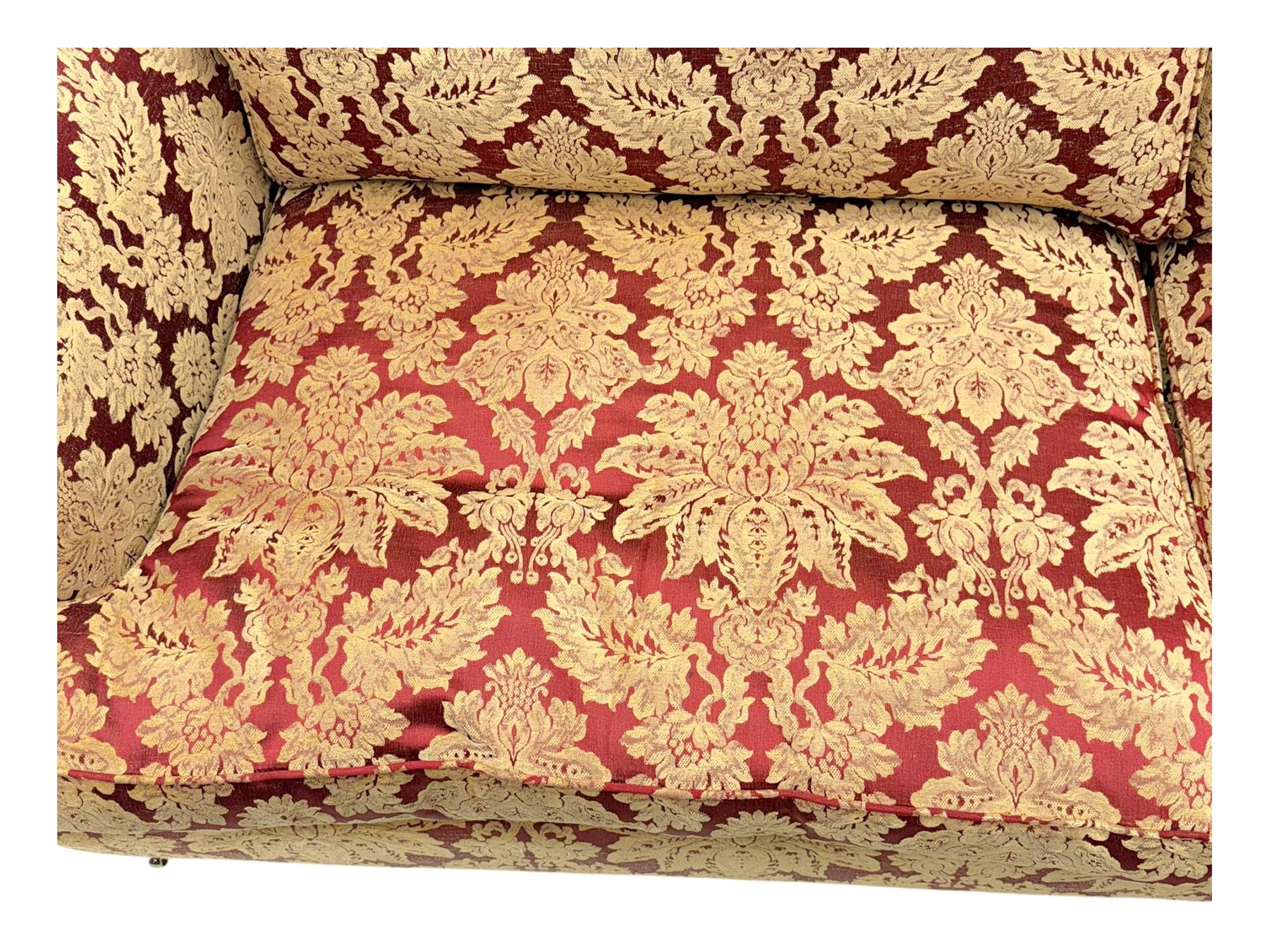 Duresta - pair of Grande three-seat sofas, traditional shaped with rolled arms and upholstered loose cushions, in red ground fabric with raised gold foliate pattern, on turned feet with brass castors 