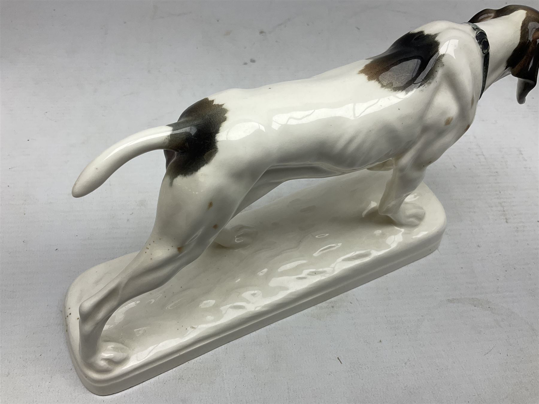 Early 20th century Katzhütte figure of a pointer dog, and figure of a young girl holding basket and fan, both with green cat H house printed mark beneath, dog L25cm