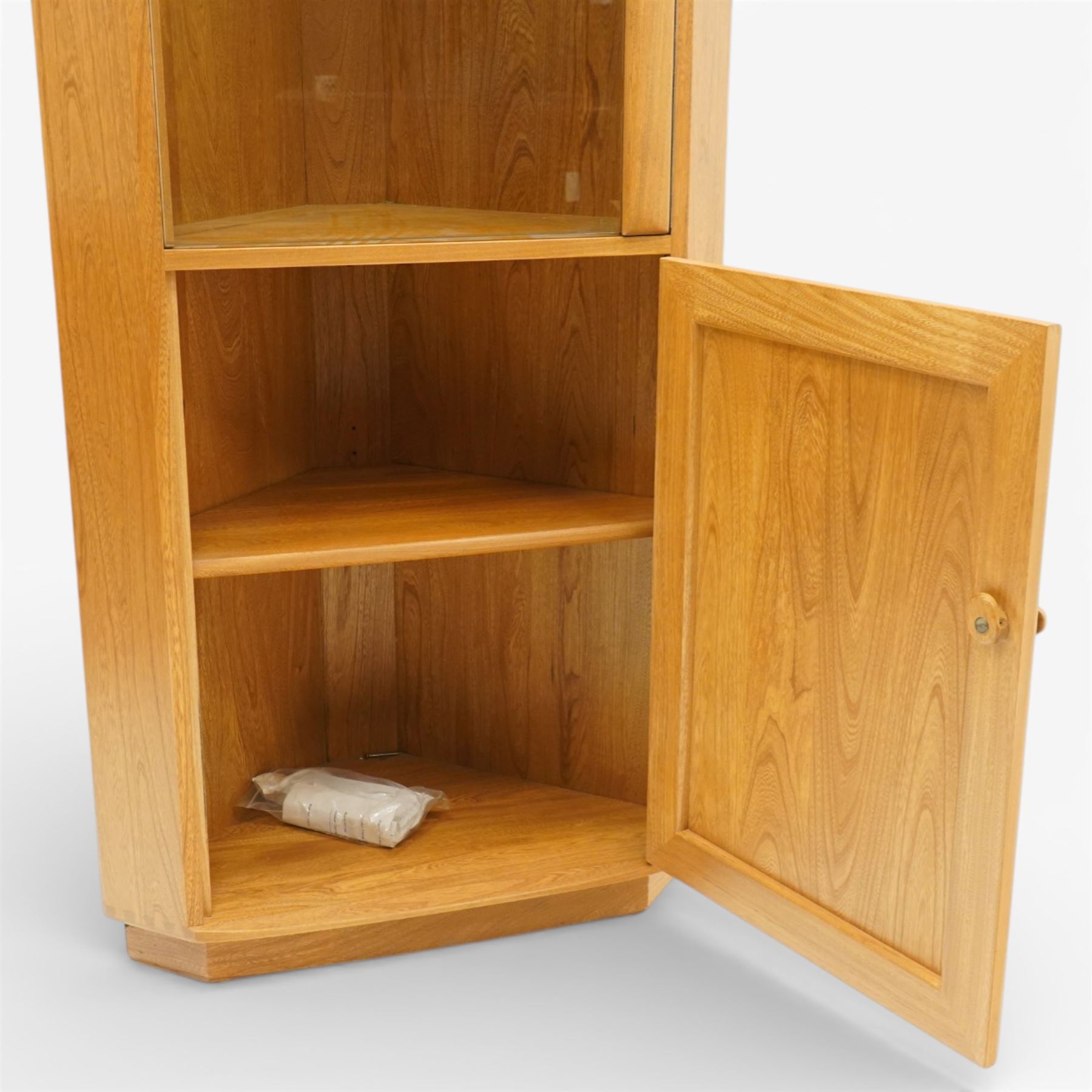 Ercol - elm corner display cabinet, Model 3856. Glazed upper section with glass door enclosing two glass shelves and interior light, above panel cupboard door, with rounded uprights and circular turned handles, on plinth base