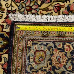 Fine Qom hand-knotted rug, ivory ground, with a dark navy shaped floral medallion and pendants, the field densely worked with fine flowering vines, palmettes and leafy scrolls in red, green, ochre and blue tones, within golden spandrels and a dark navy floral border, flanked by narrow guard stripes, with cotton fringes