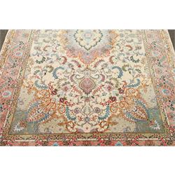 Fine Persian silk inlaid ivory and rose ground Tabriz rug, the busy field decorated with a central foliate pole medallion surrounded by scrolling foliage with trailing flowerheads and bouquets, the multiple guard lines filled with repeating scrolling palmettes and interlocking floral motifs