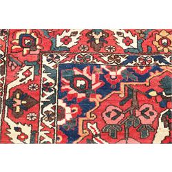 Vintage Persian Heriz crimson ground rug, the field decorated with a central stylised urn and bird of paradise motifs, the guard  lines with repeating stylised plant motifs of geometric form