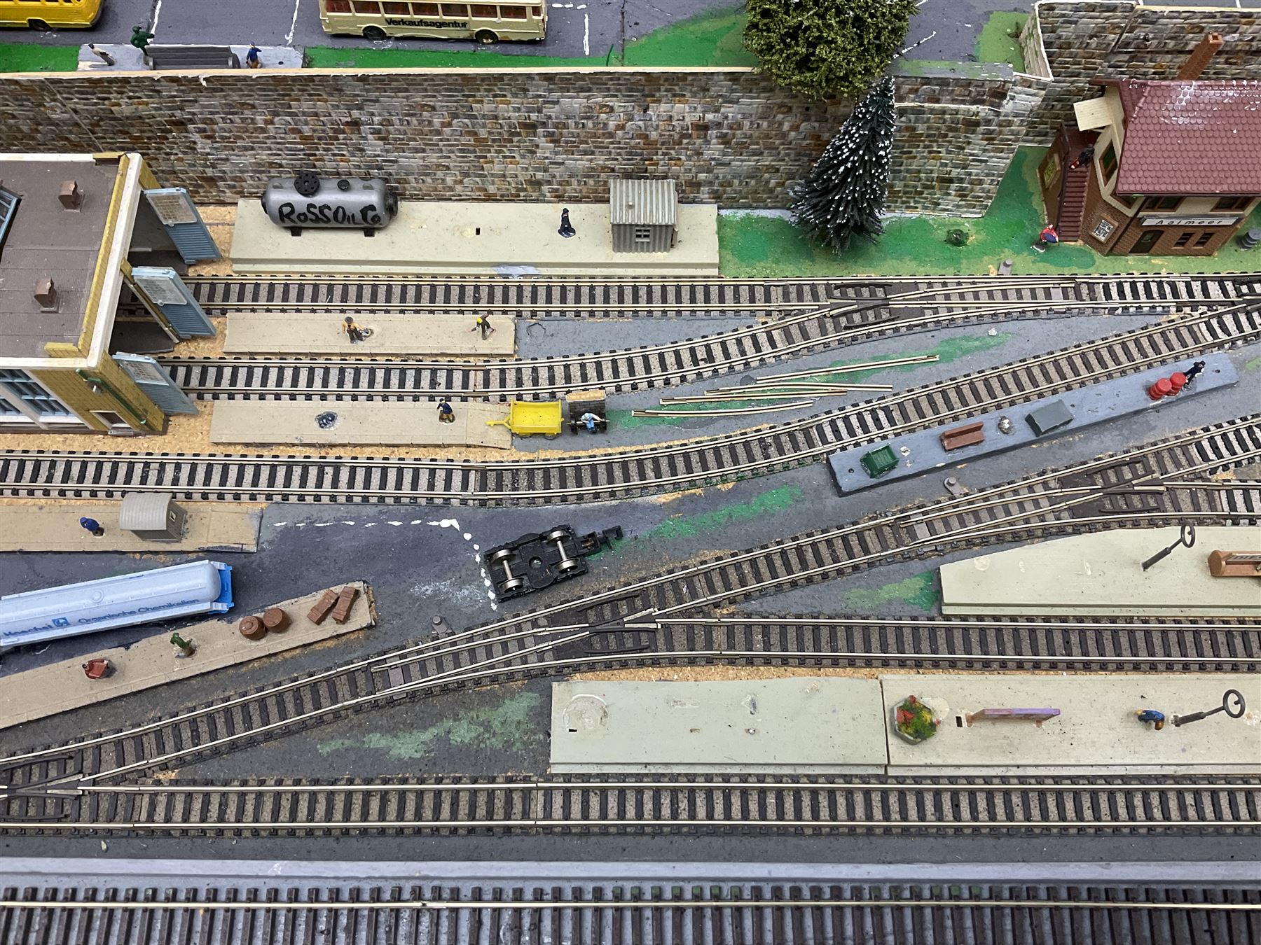 Table top 'N' gauge continental scenic layout as a split level town with various loops of track, station with numerous platforms, engine shed, assorted buildings, roads with motor vehicles and figures, tunnels, trees, river with bridge, tram depot etc 122 x 52cm