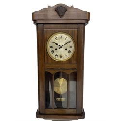 1930s wall clock in an oak case with a crested pediment and glazed door with visible pendulum, silvered dial with Roman numerals and steel spade hands, eight day spring driven movement striking the hours and half hours on a gong. With pendulum and key.