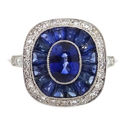  Platinum (tested) ring set with central oval sapphire, halo of calibre cut sapphires and a diamond surround, with diamond shoulders  