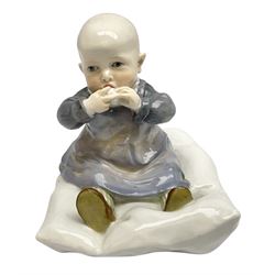 Early 20th century Meissen figure, circa 1905-1924, designed by Konrad Hentschel, modelled as a baby seated upon a cushion wearing a merging purple and blue dress, green and white striped leggings and brown shoes, with blue crossed swords mark and incised model number U 150 beneath, H12.5cm

