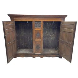 Large 18th century and later oak livery cupboard, projecting moulded and dentil cornice, sunken fillet moulded frame, triple vertical panelled central upright, enclosed by two doors each with five panels, the top row of panels carved with stylised scrolls, the lower panels carved with foliate lozenges, on shaped bracketed skirt base 