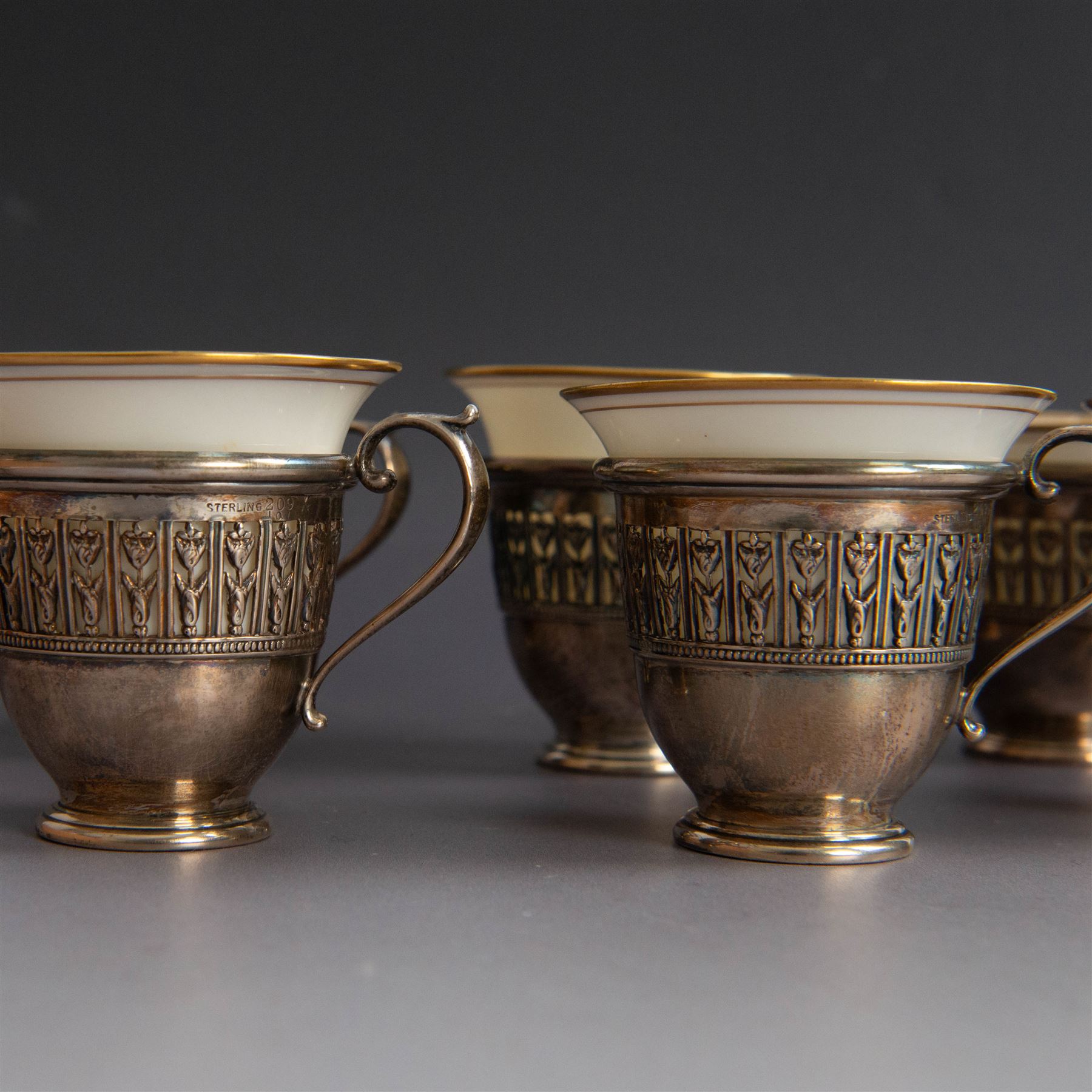 Set of six Lenox porcelain coffee cups, with gilt rims, each with American silver openwork cup holders, stamped sterling